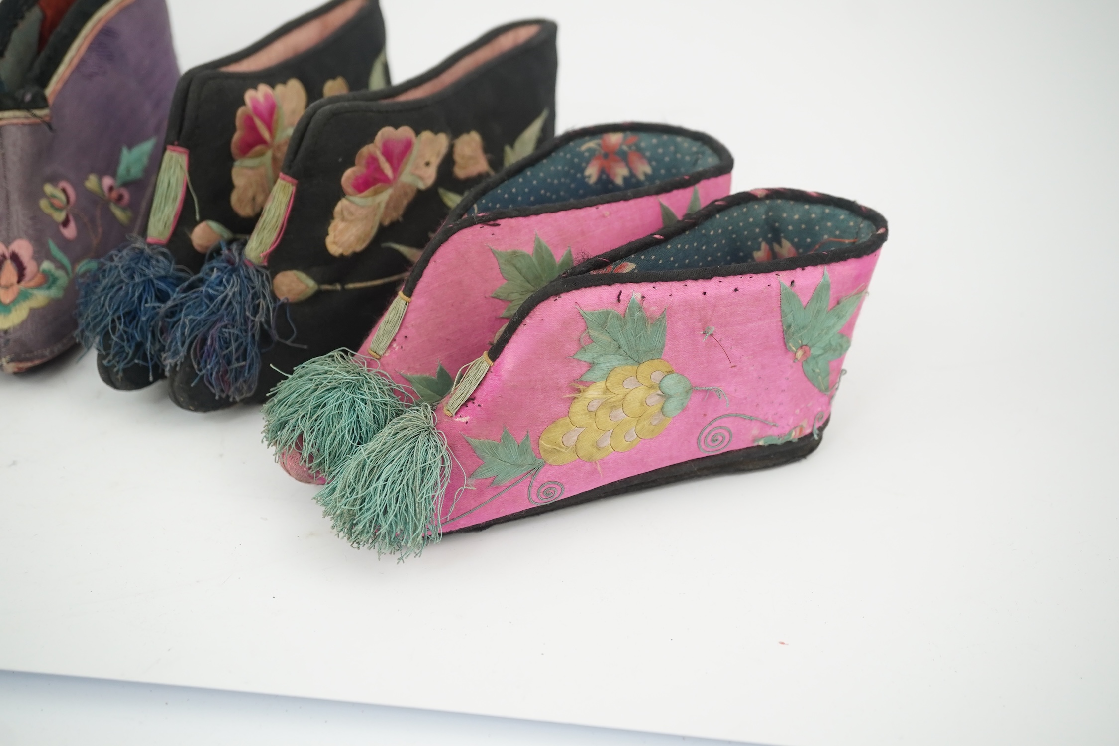 Four pairs of late 19th / early 20th Chinese ladies bound foot shoes, made in various coloured silks, with colourful floral embroidered motifs, two pairs with decorative silk pom-poms and another made of purple and black